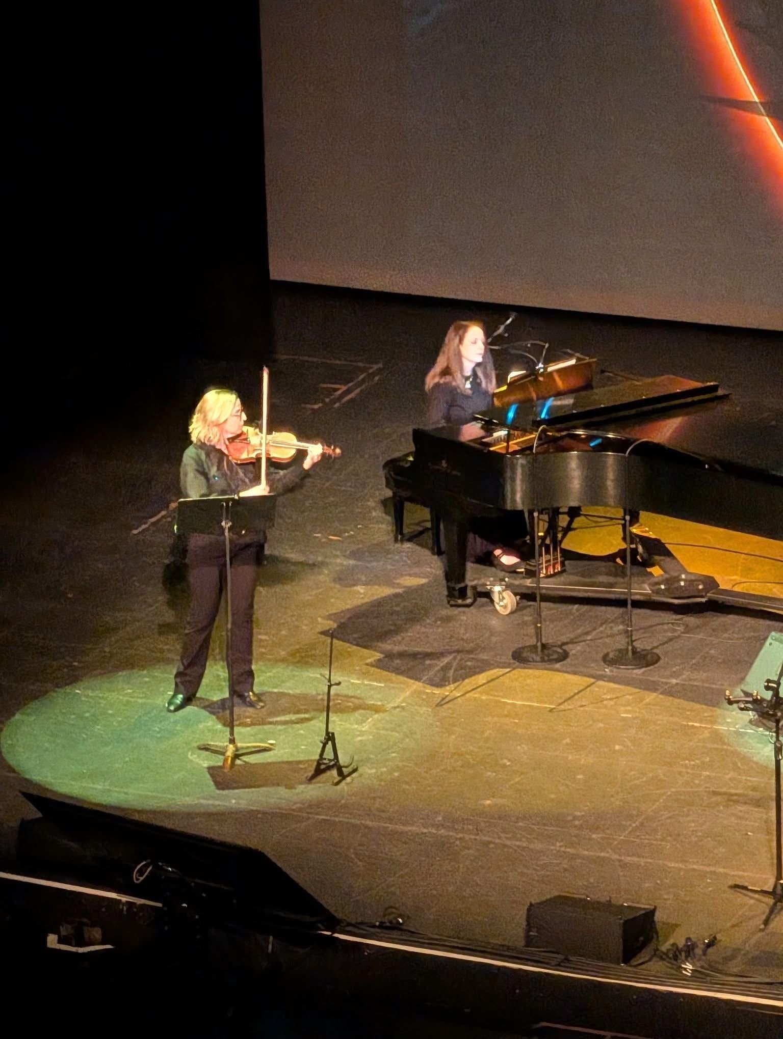 Gretel performing violin on stage with a pianist